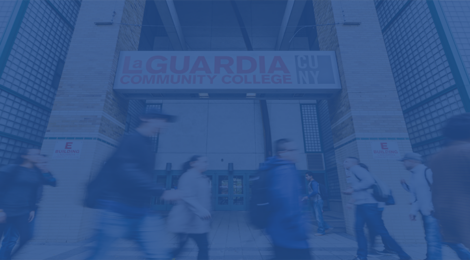 Students walking by the entrance of the E building under the LaGuardia Community College logo.